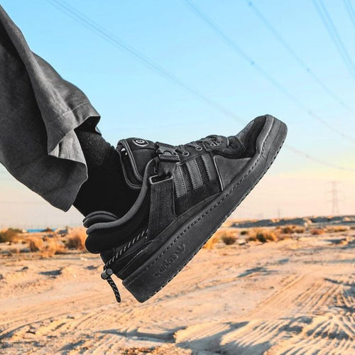 Hierbij biedt JSYS (justshopyourshoes) de zwarte schoen 'Adidas Forum Buckle Low Bad Back To School' Dit wordt gedaan door de schoen te fotograferen, waarbij iemand zijn voet optilt in de woestijn. 